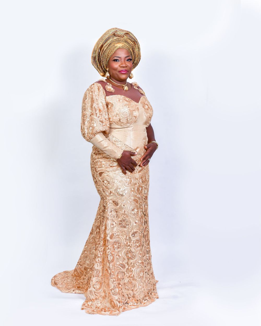 Woman in gold lace mermaid gown and matching gele posing gracefully.