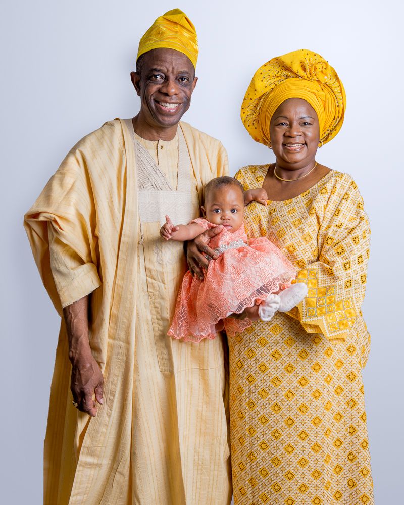 Nigerian grandparents in yellow traditional attire holding baby in peach dress.