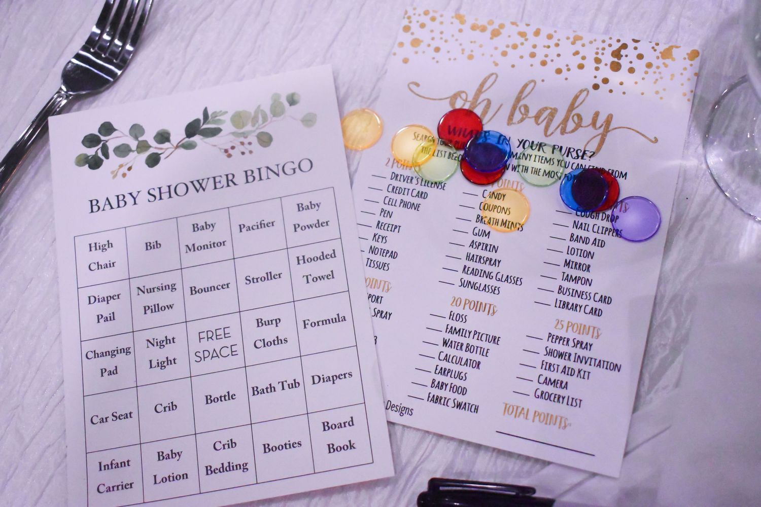 Baby shower bingo and oh baby party game cards displayed on a white table at a celebration.