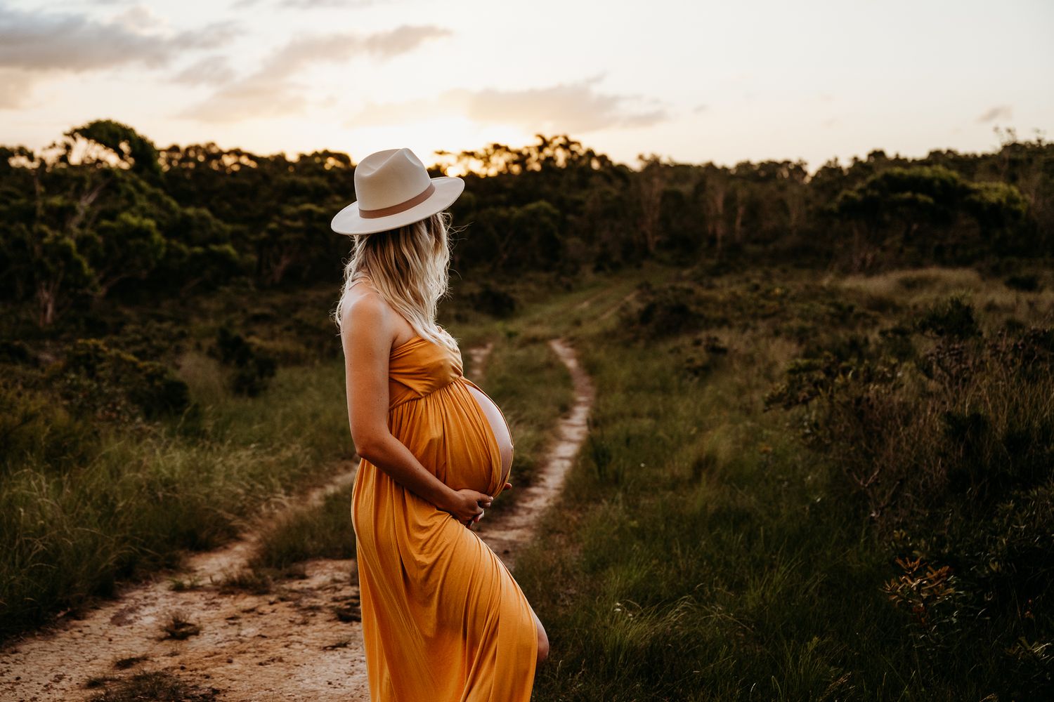 A sunset maternity photo in a golden dress on a winding dirt path.