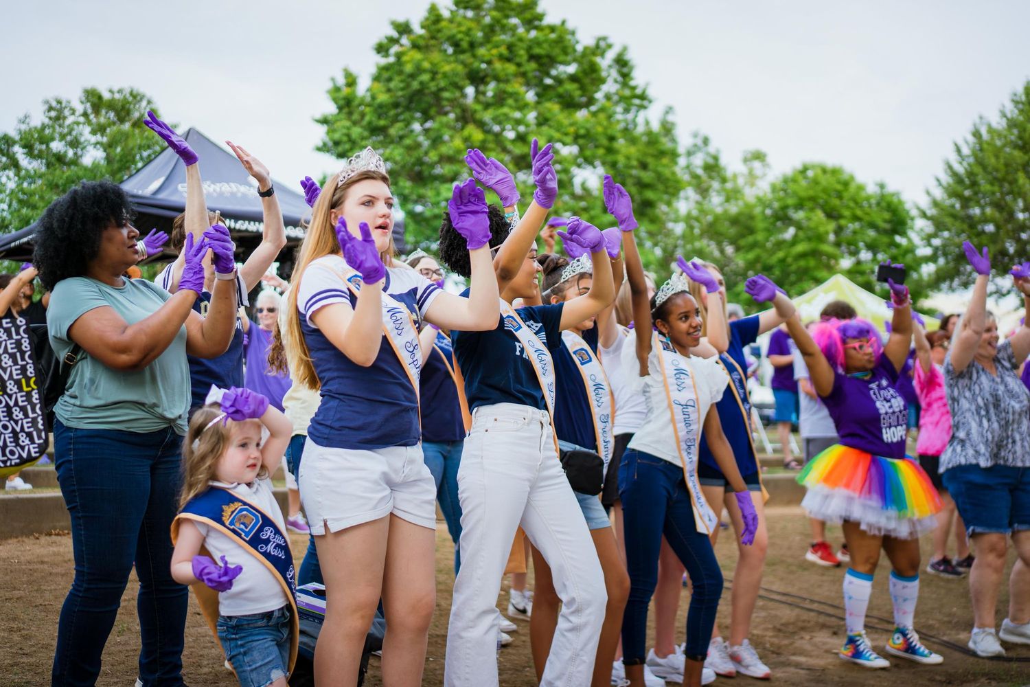 men, woman, and children dancing with purple gloves on celebrating the fight against cancer
