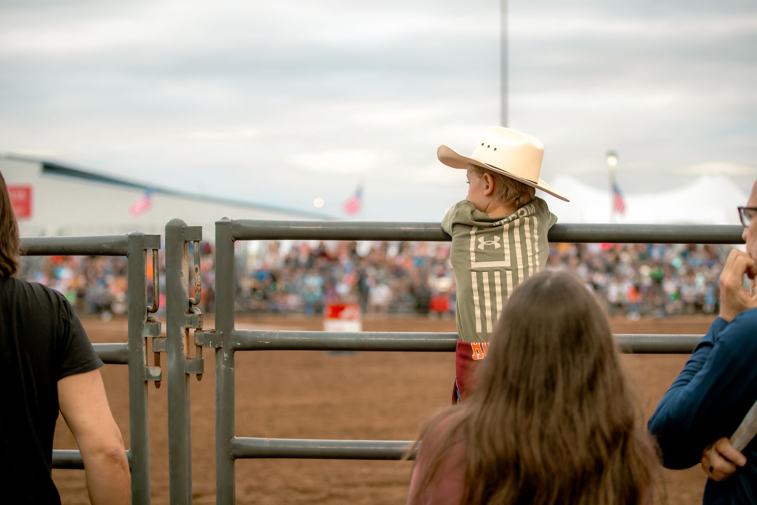 Spectators watching rodeo event through metal barriers at outdoor arena.