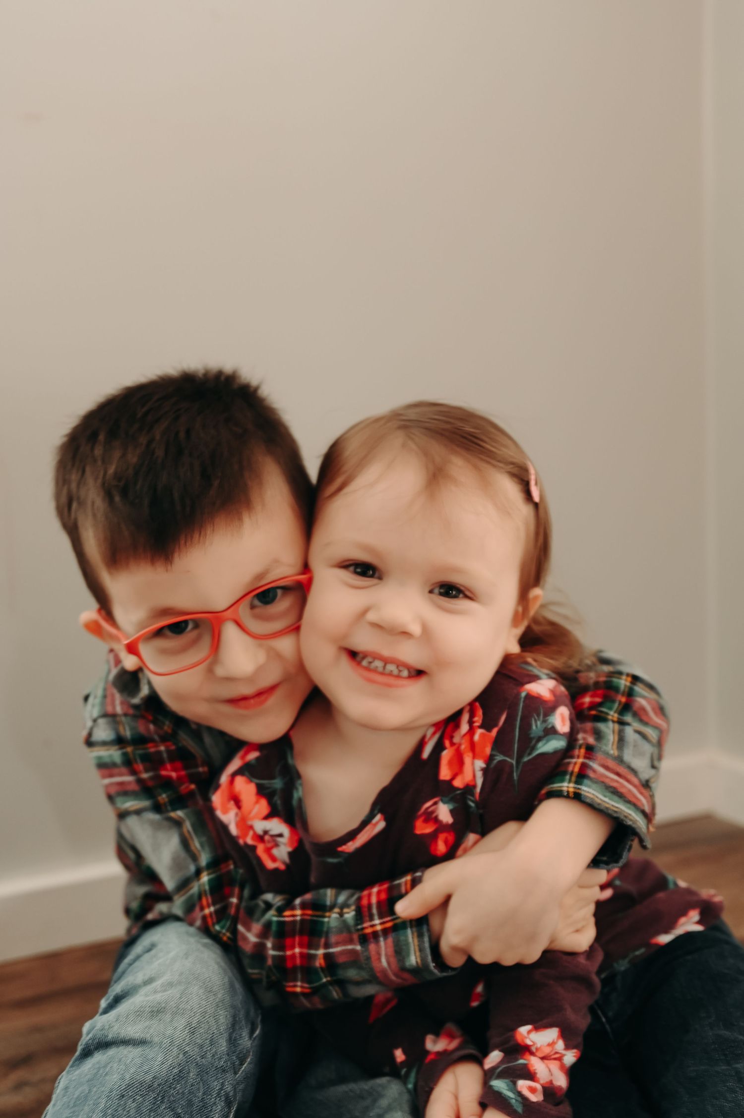 Two siblings in matching plaid shirts share a sweet embrace and smile together.