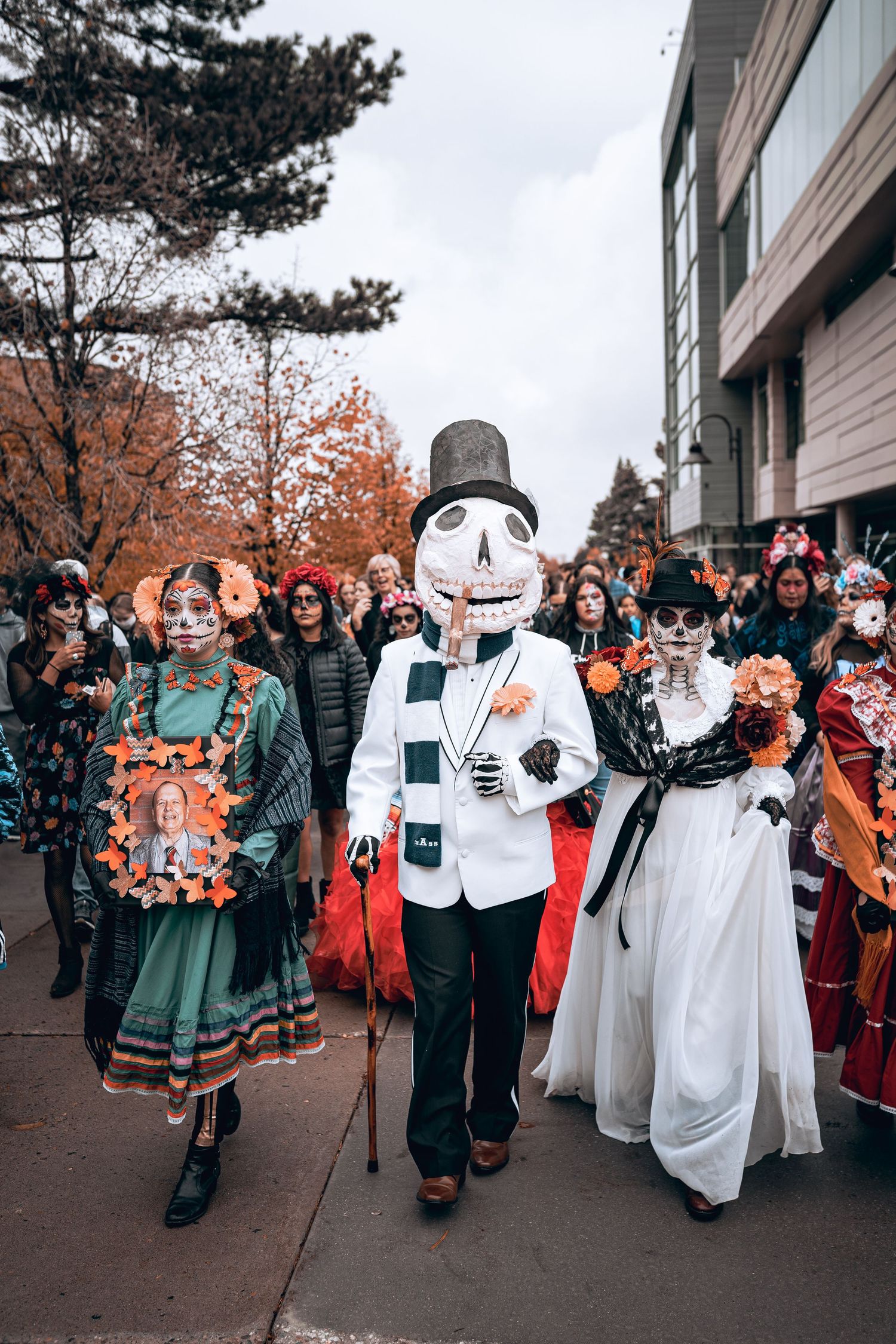 Halloween parade with people in costumes including a tall figure in a skeleton mask and top hat.