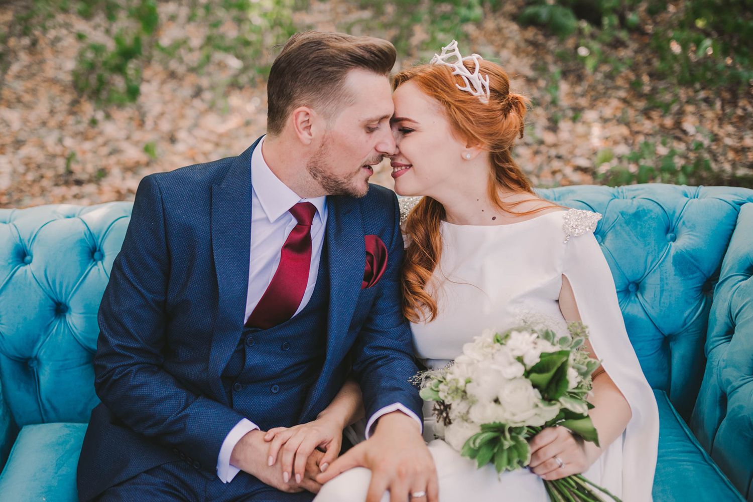 A tender wedding moment captured in a forest setting with a turquoise vintage couch.