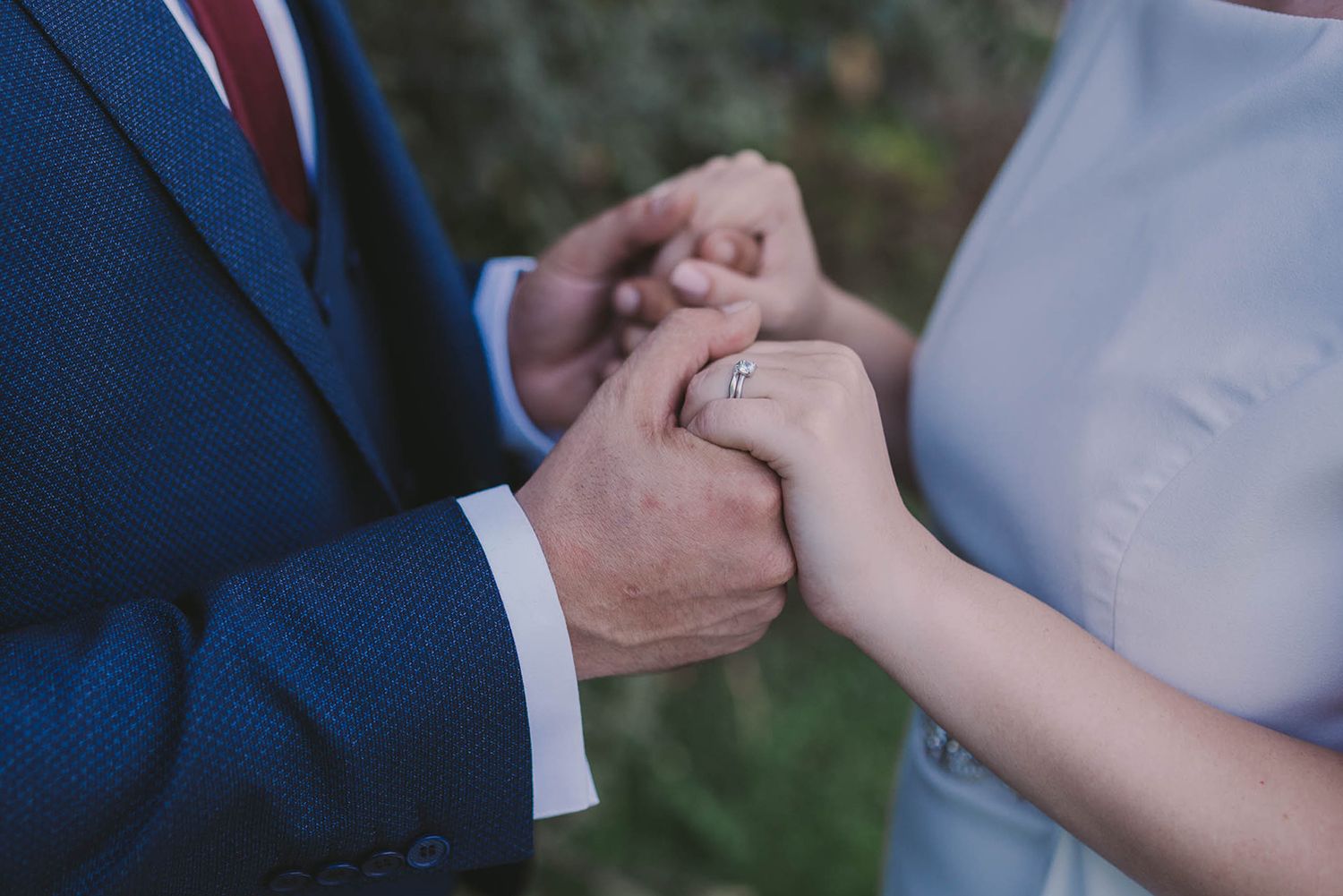 Close-up of hands exchanging wedding rings during an outdoor ceremony.