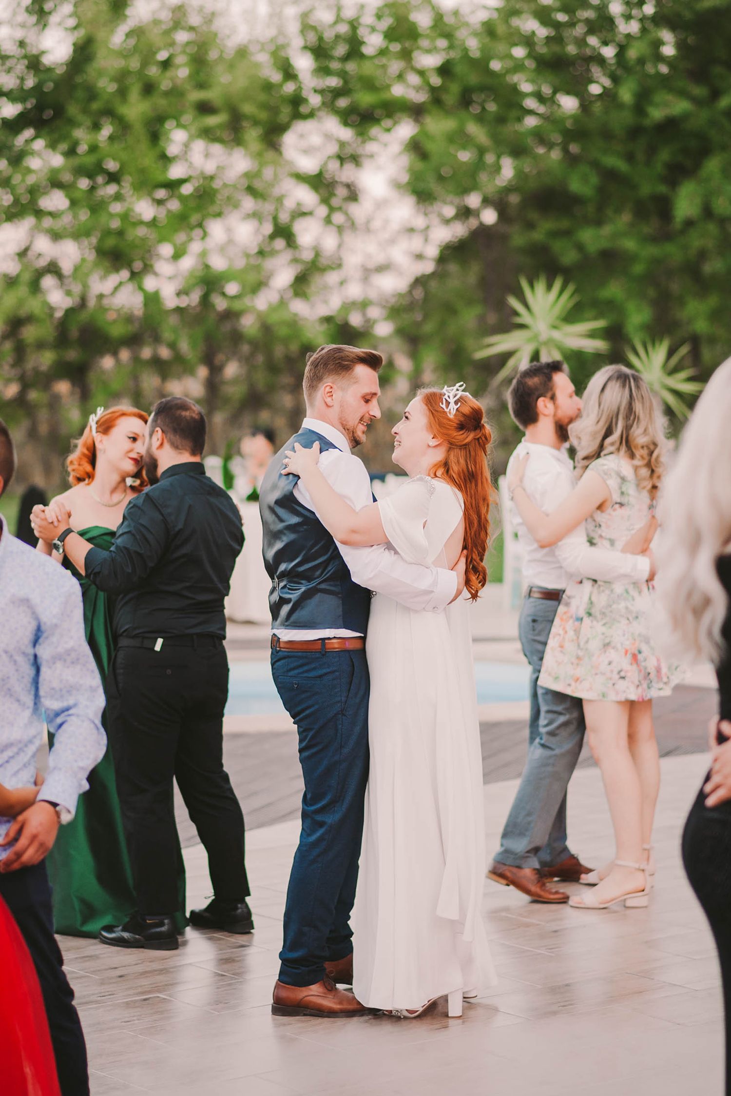 Wedding guests dance in pairs on an outdoor patio during reception festivities.