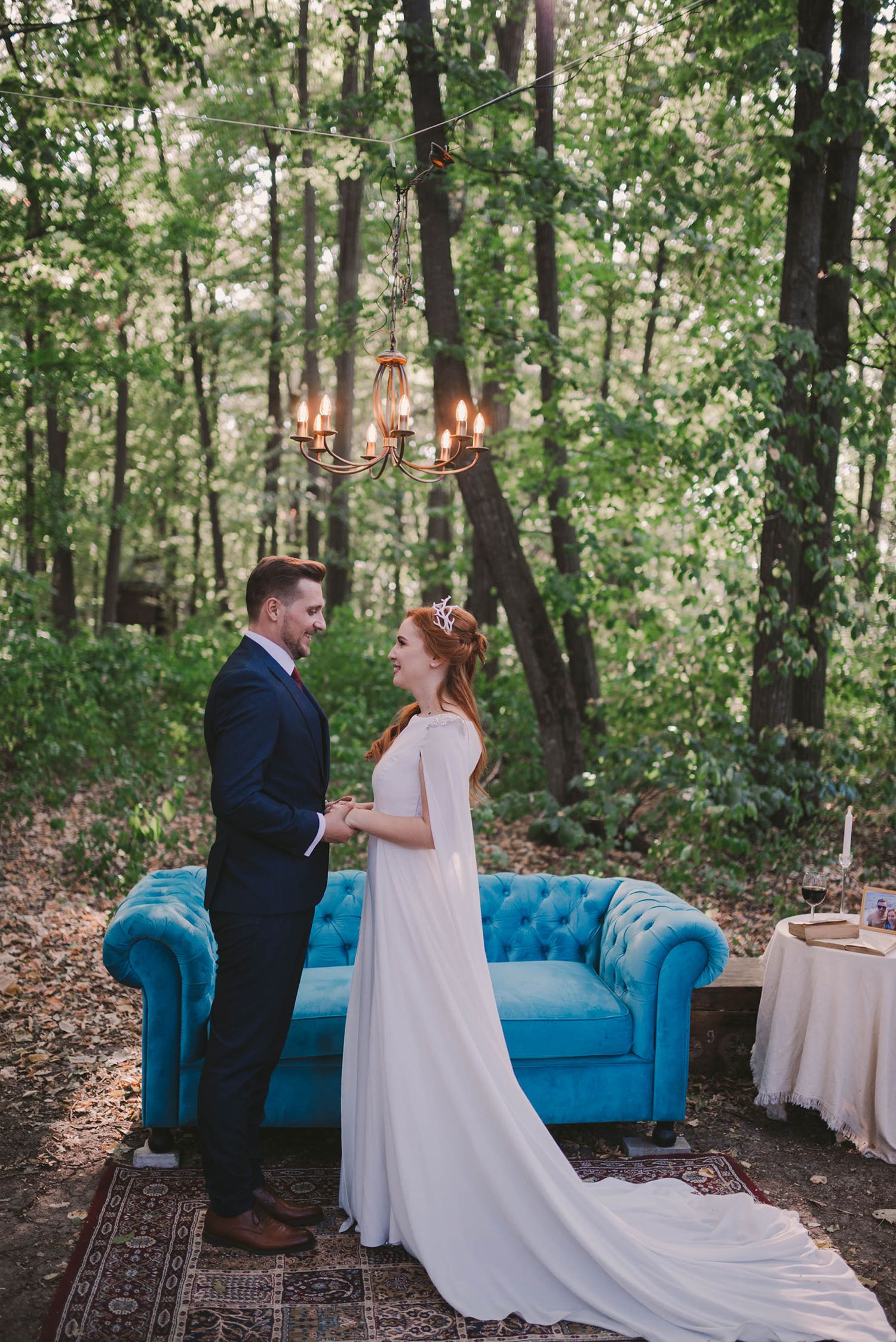 An outdoor woodland wedding scene featuring a tufted blue velvet sofa and oriental rug.