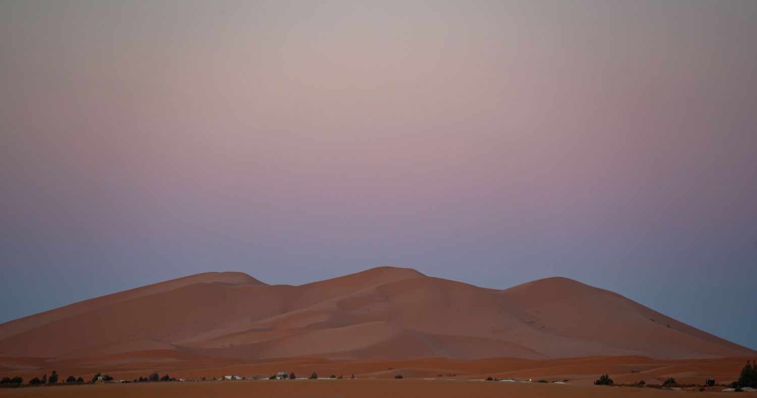 Desert sand dunes at twilight with pink and purple sky.