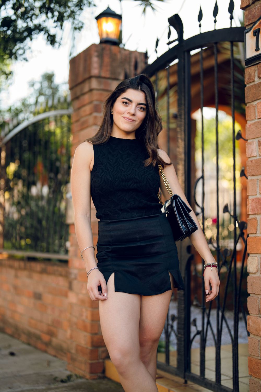 Fashion portrait session outdoors with brick wall and iron gate backdrop in casual black attire.