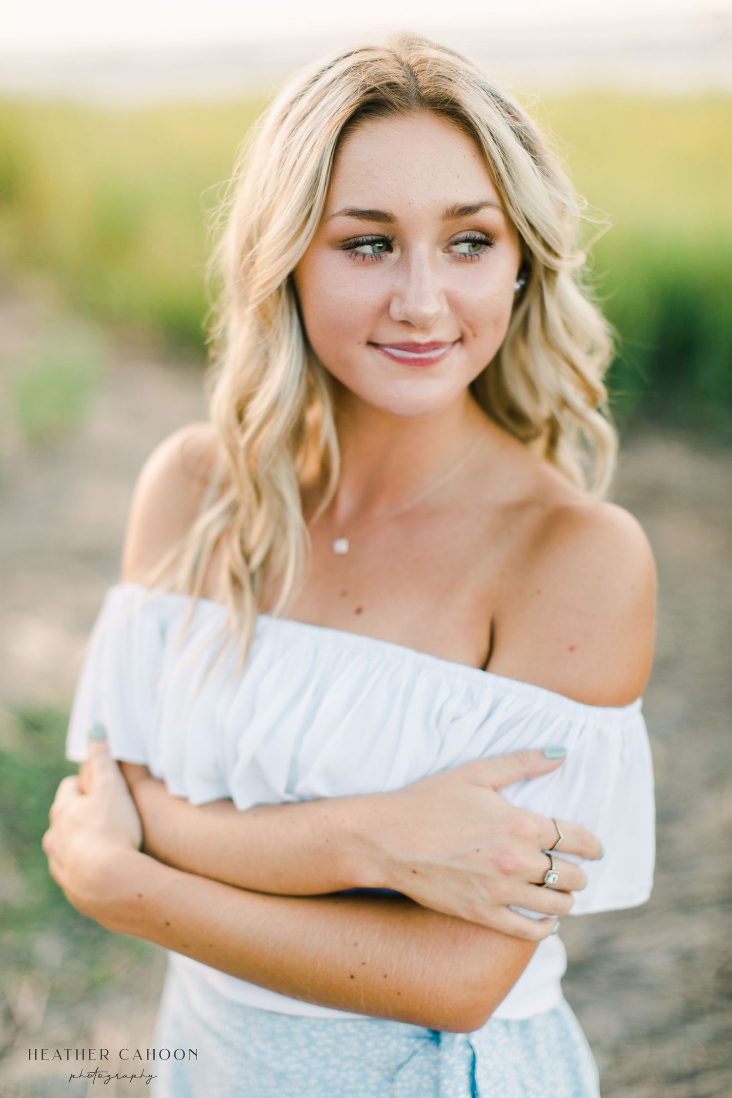Portrait of woman in white off-shoulder top against blurred natural background.