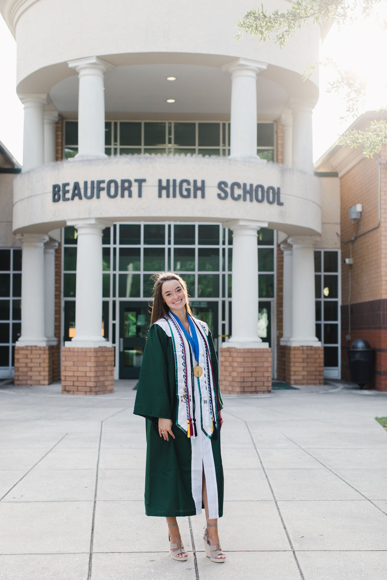 Graduate in green cap and gown poses in front of Beaufort High School entrance.