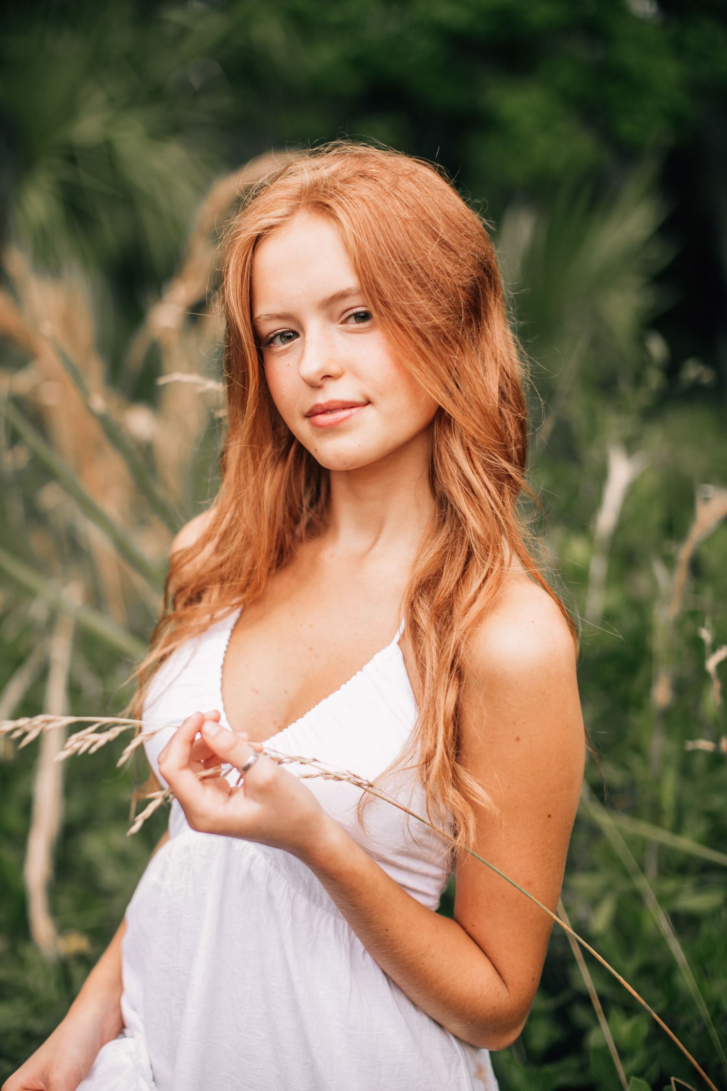Portrait in tall grass wearing white sundress with natural lighting.