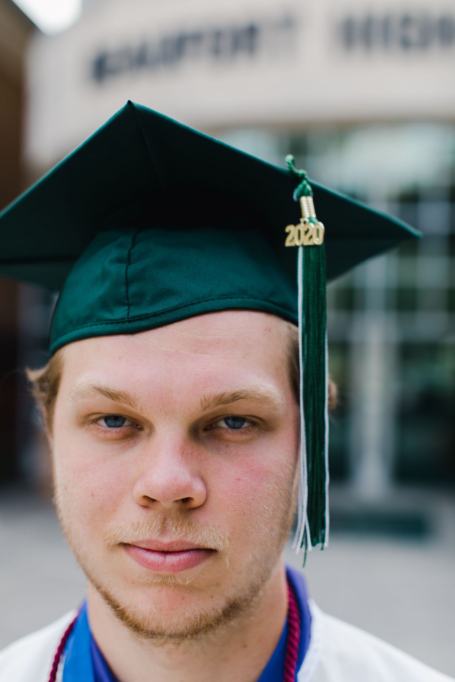 Beaufort high school graduate in dark green cap with gold tassel poses in front of school building posing for senior photos.
