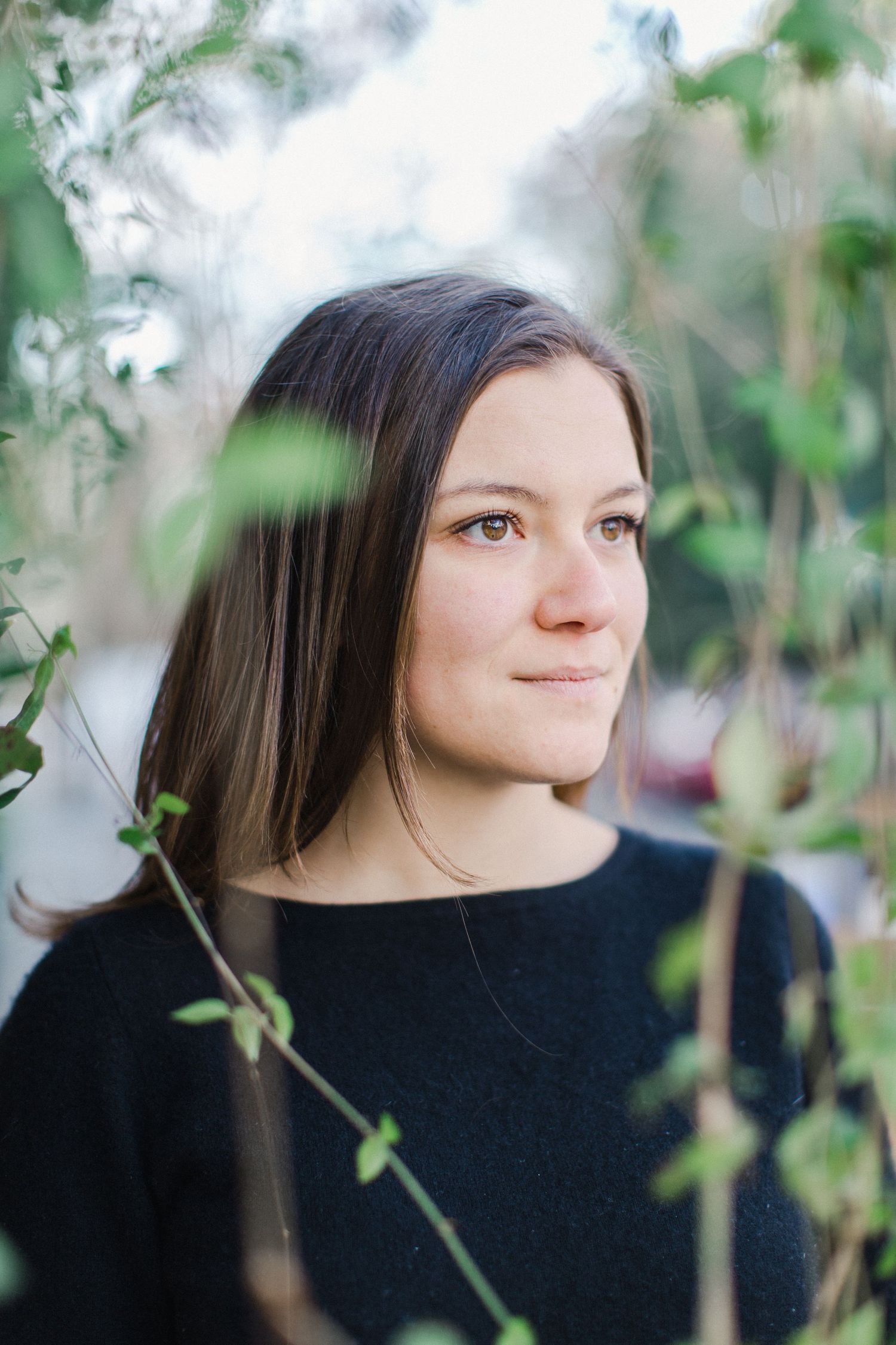 Artistic portrait of woman in black sweater framed by green foliage.