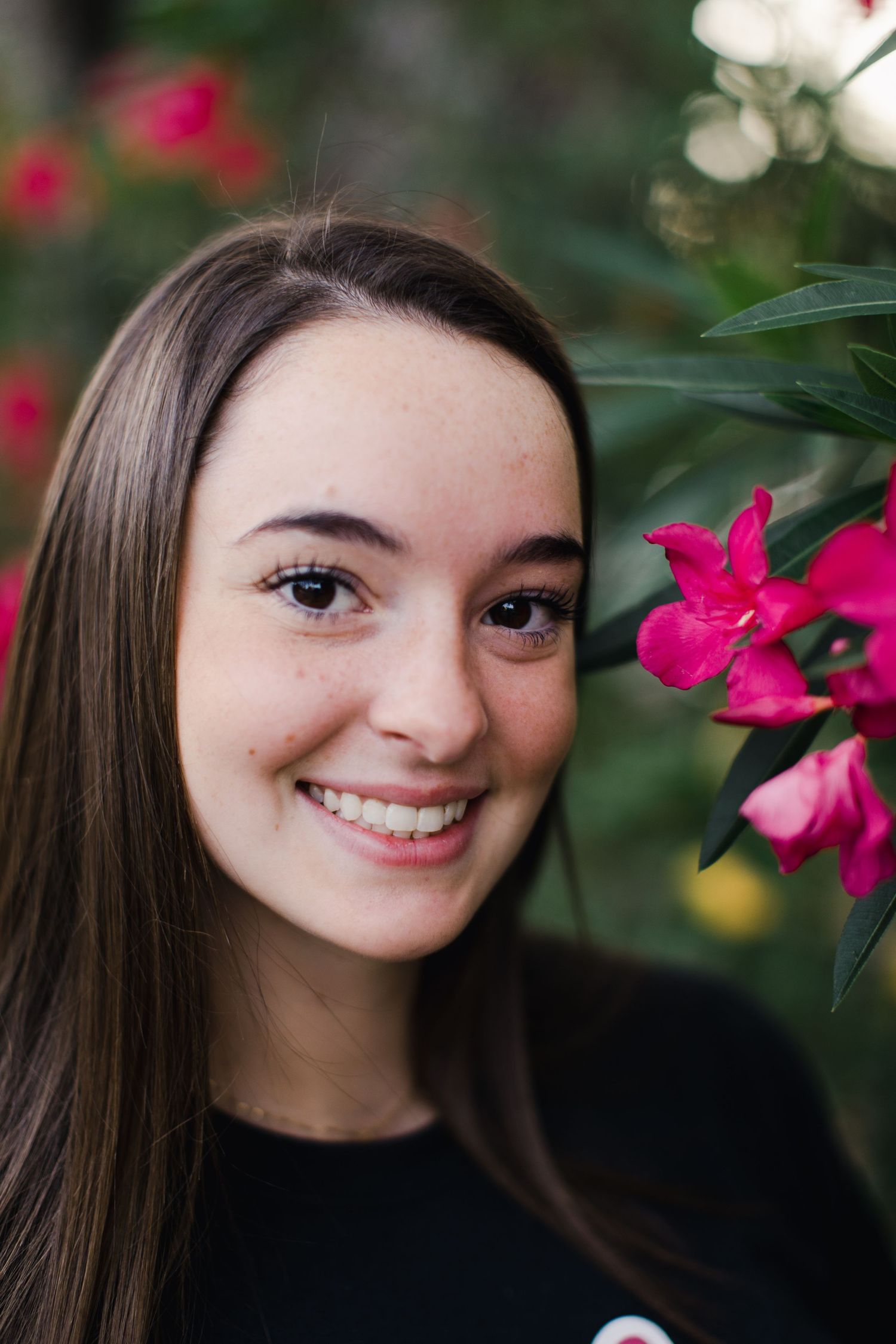 Portrait of a student with long brown hair smiling next to bright pink flowers.