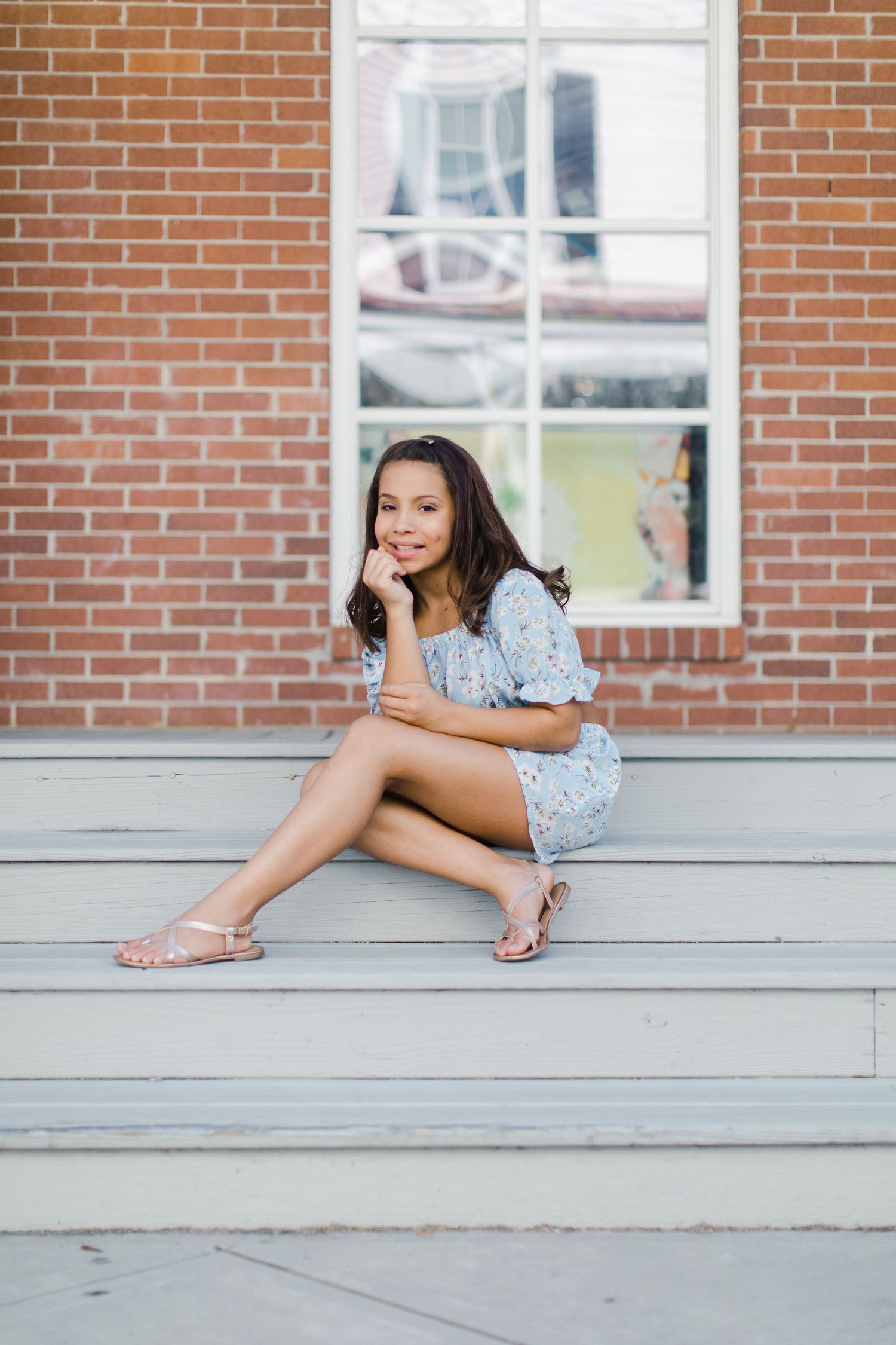 Person in blue floral outfit sitting on gray steps near brick wall.