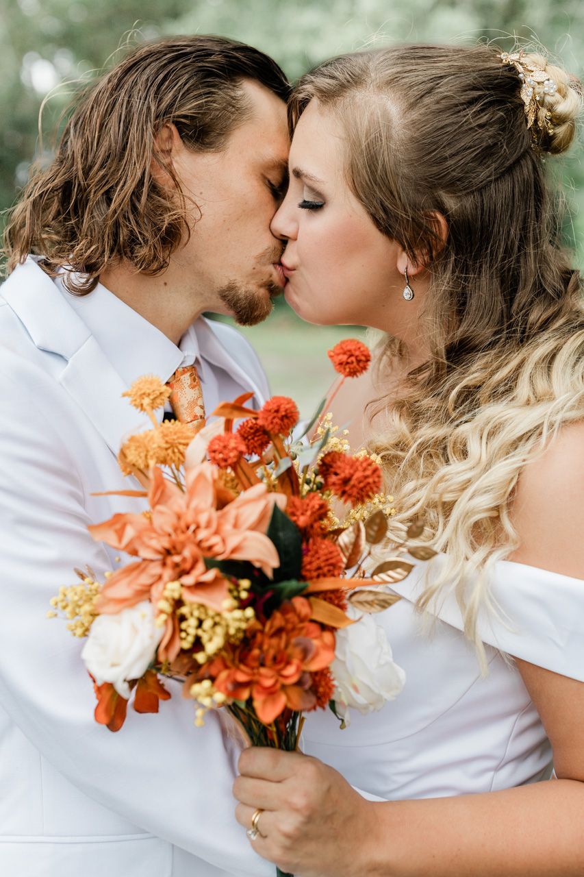 A romantic couple in white sharing intimate moments with orange flowers.