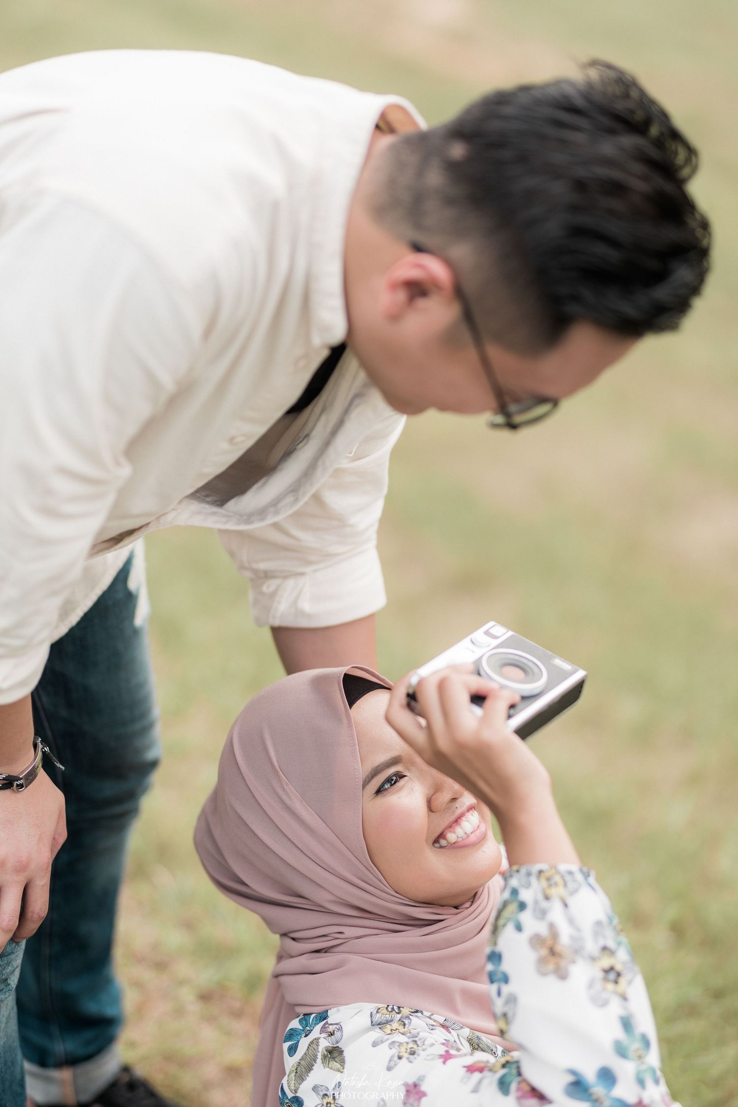 A romantic outdoor photoshoot showing playful interactions between a couple on grassy terrain.