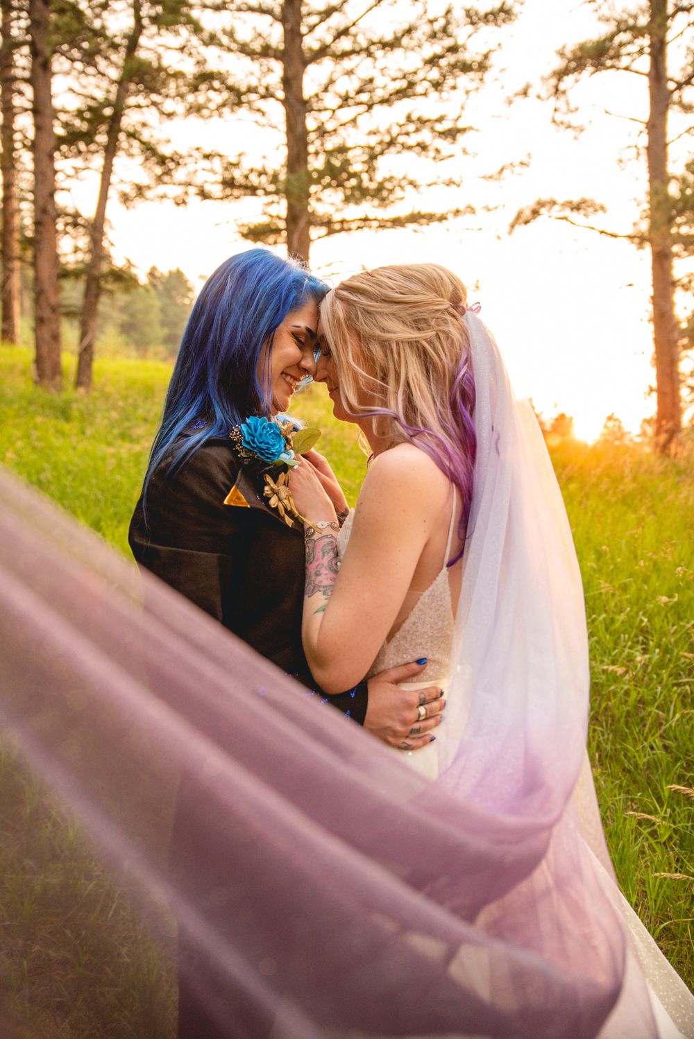 A romantic wedding moment at sunset with colorful hair and flowing veil in a forest setting