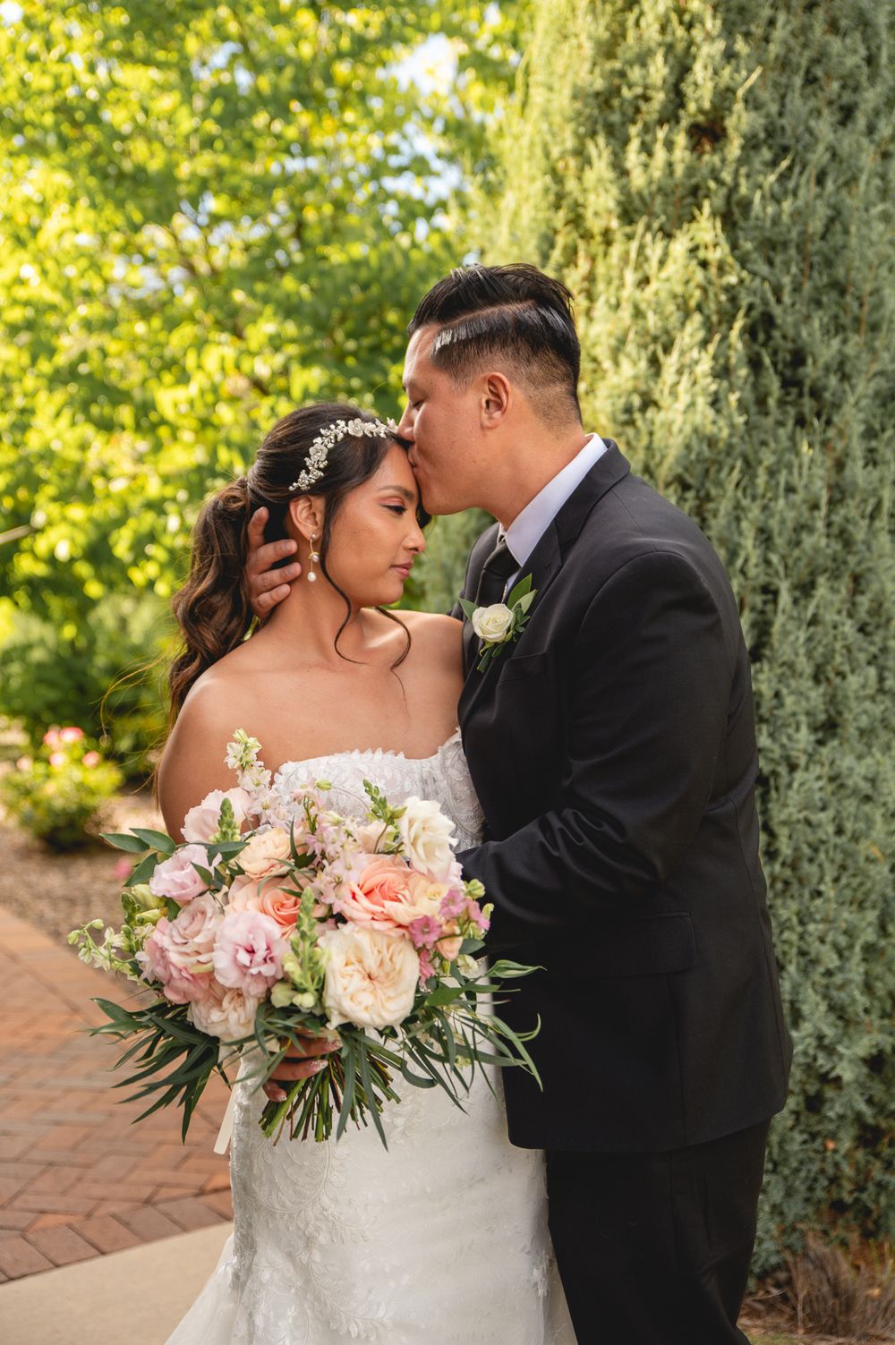 A tender wedding moment outdoors with a bride holding a lush pink and white bouquet against a garden backdrop.