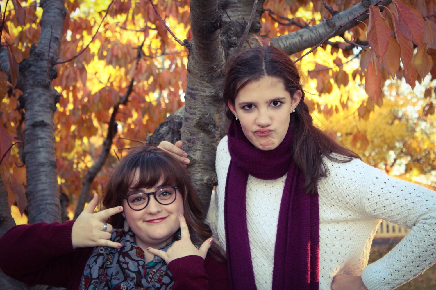 Two people pose together against autumn trees with golden leaves.