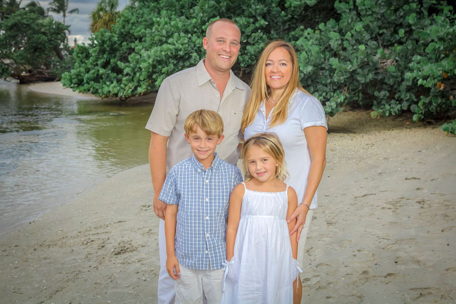 Family of four posing together on the sand by the water