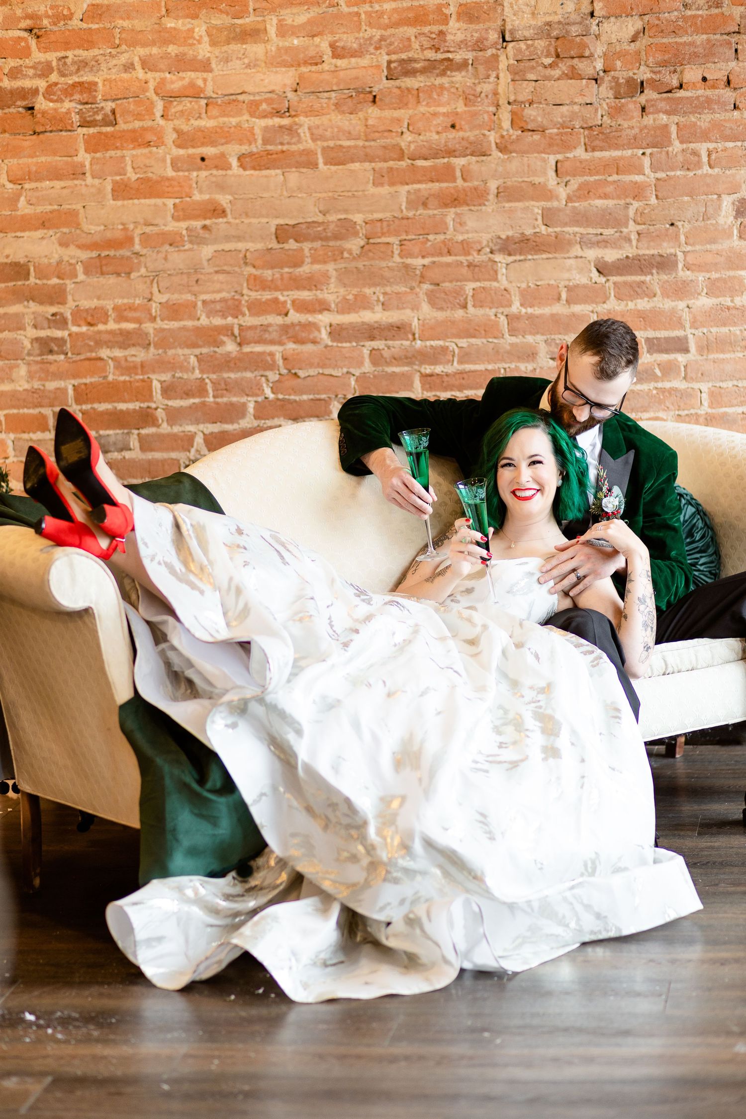Bride and groom lounge on sofa sipping champagne
