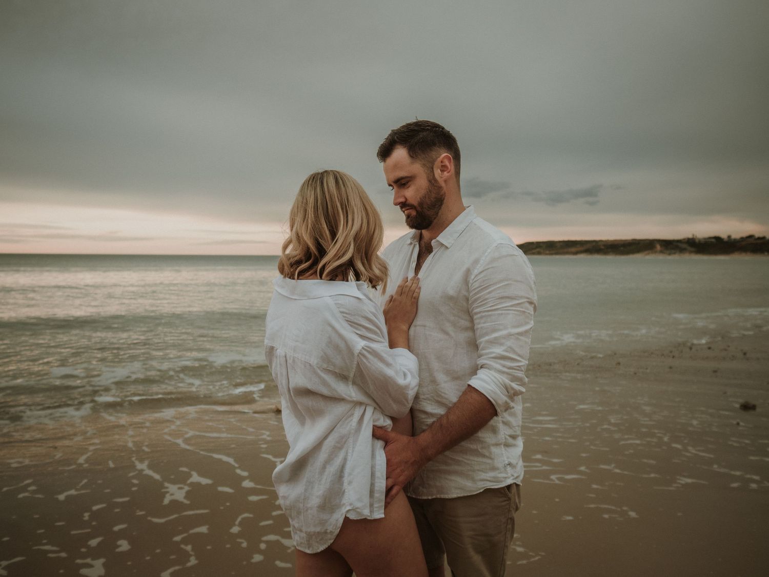 A moody beach portrait of a couple in white clothing during sunset.