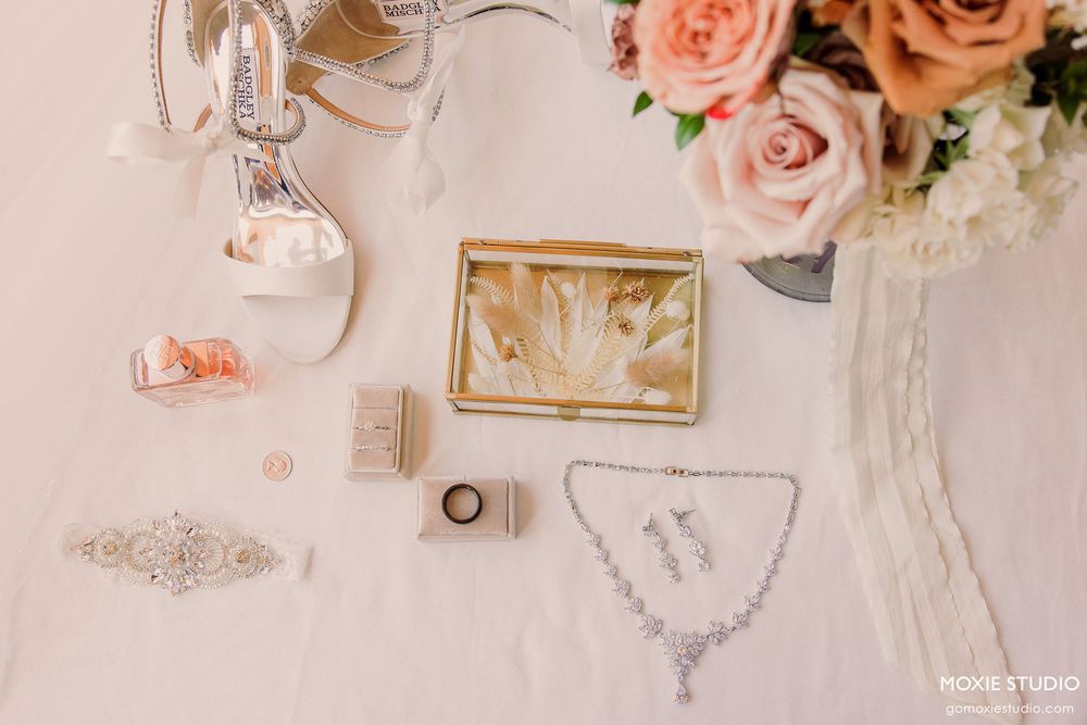 Elegant wedding details featuring pink roses, vintage keys, and delicate lace accessories arranged on a white surface.