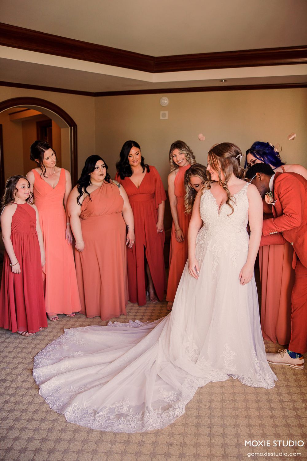 Wedding party arranged in a row showing coral bridesmaid dresses and white bridal gown with long train.