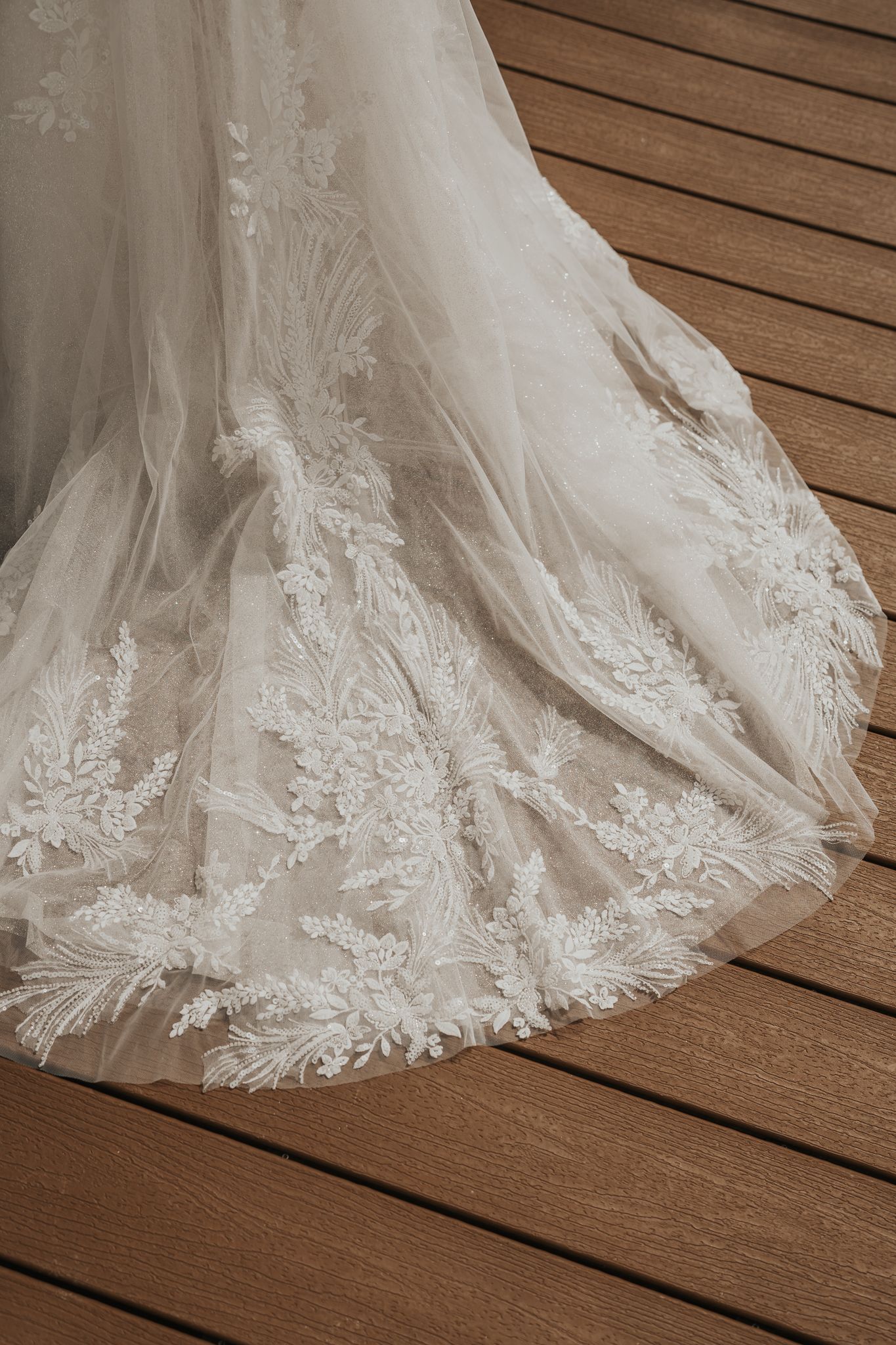 Delicate lace detail on the hem of a flowing white wedding dress against wooden floorboards.