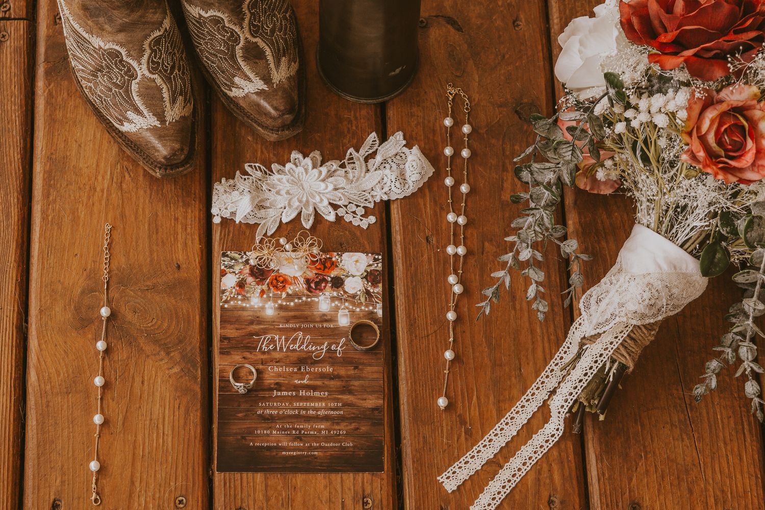 Wedding details including cowboy boots, invitation, and floral arrangements on wooden surface.