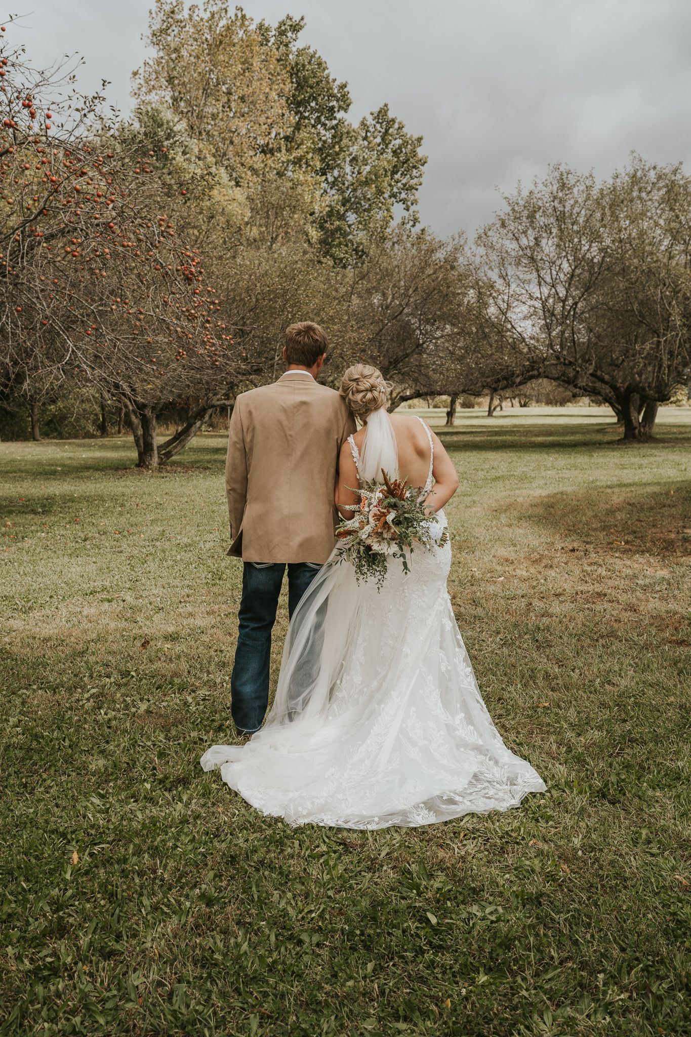 Couple walks hand in hand through an orchard on their wedding day.