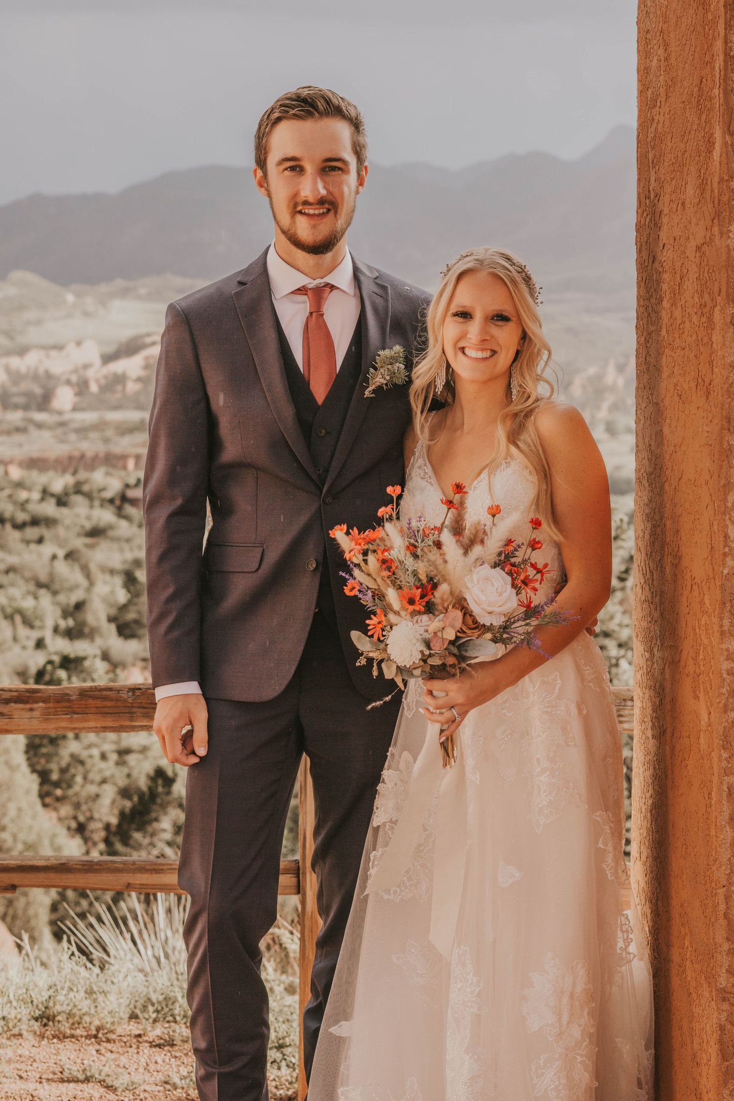 Wedding couple poses on a wooden deck with Colorado mountain landscape in the background.