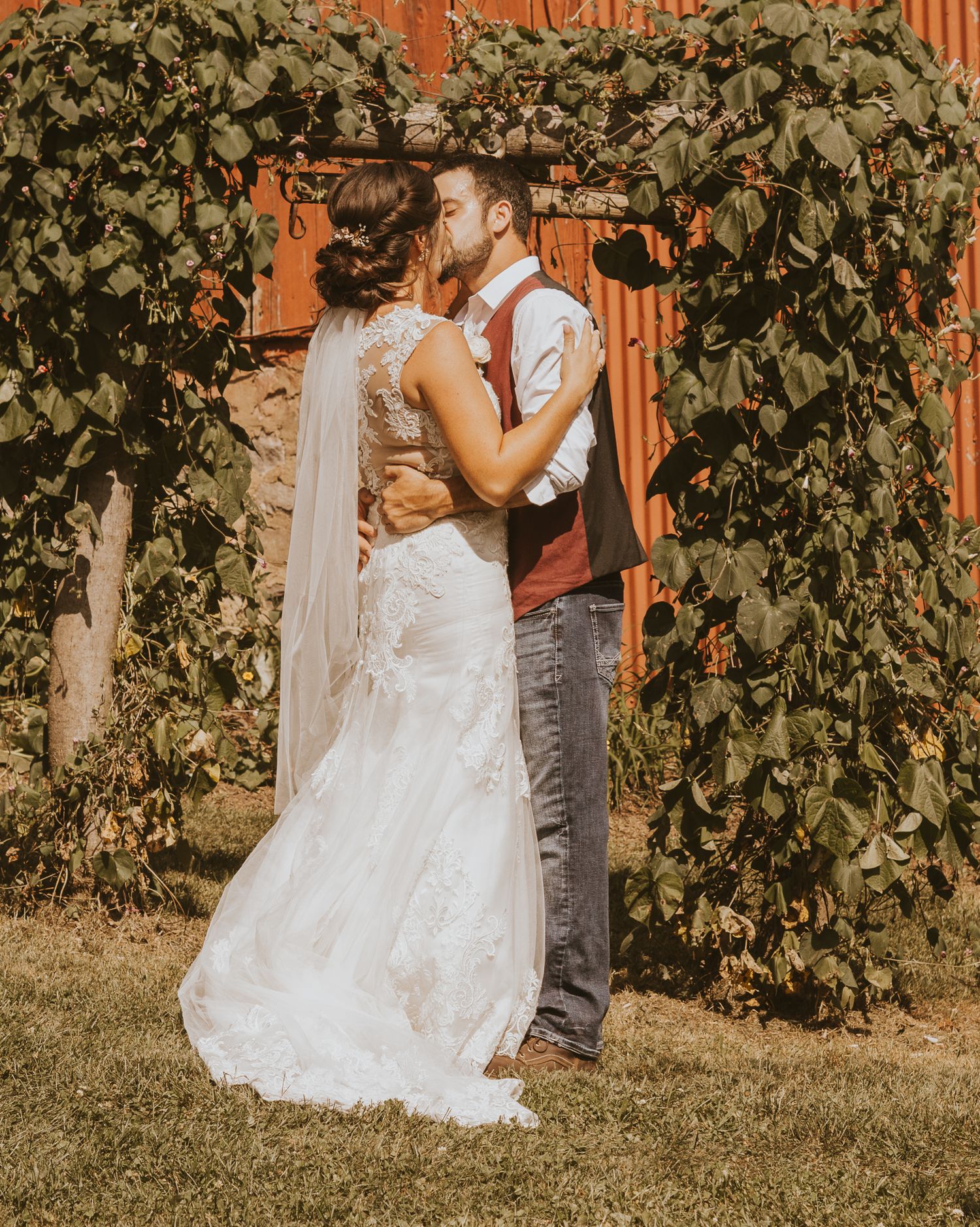 A couple shares their first kiss under a lush green archway during their wedding ceremony.