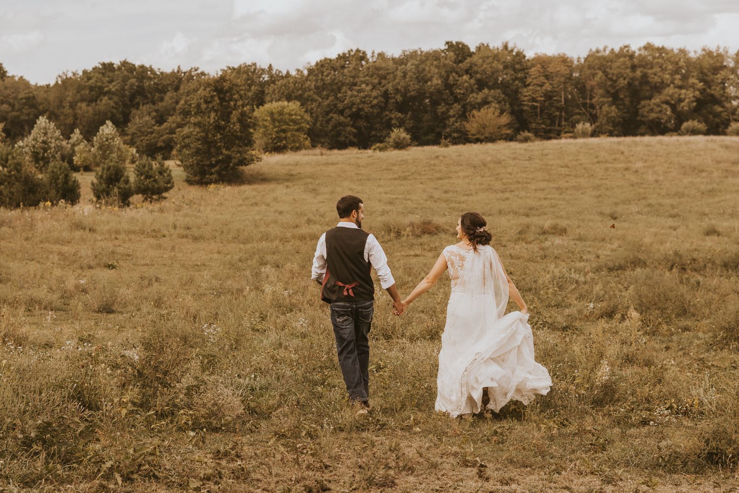 Couple walking hand in hand across scenic countryside meadow at sunset.
