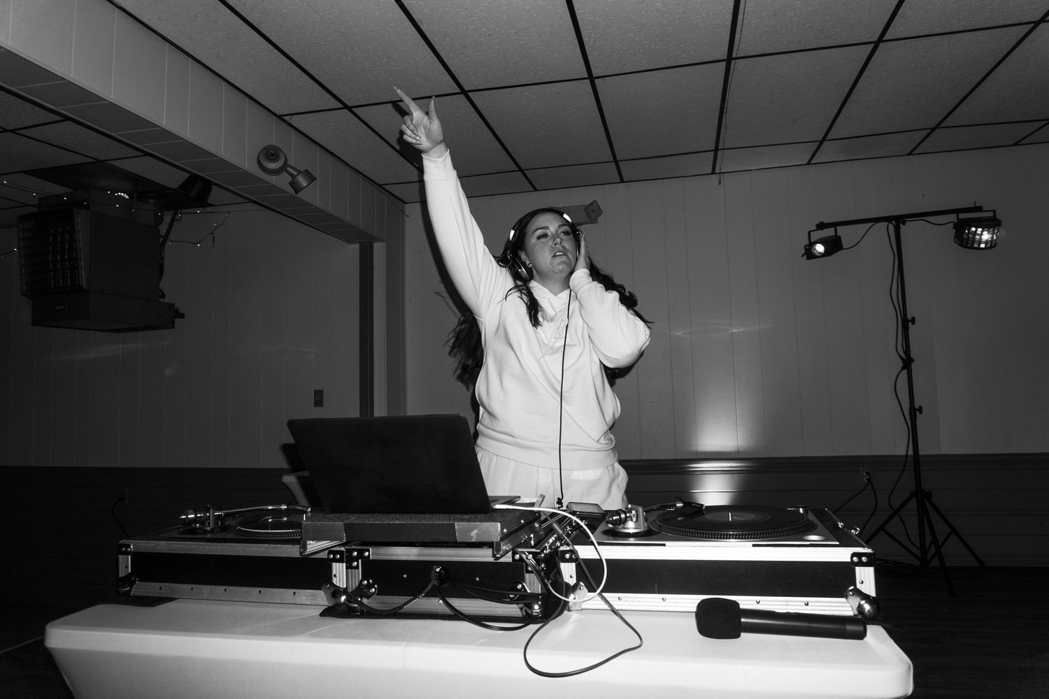 A DJ performs at a wedding reception with raised arms in black and white photography.