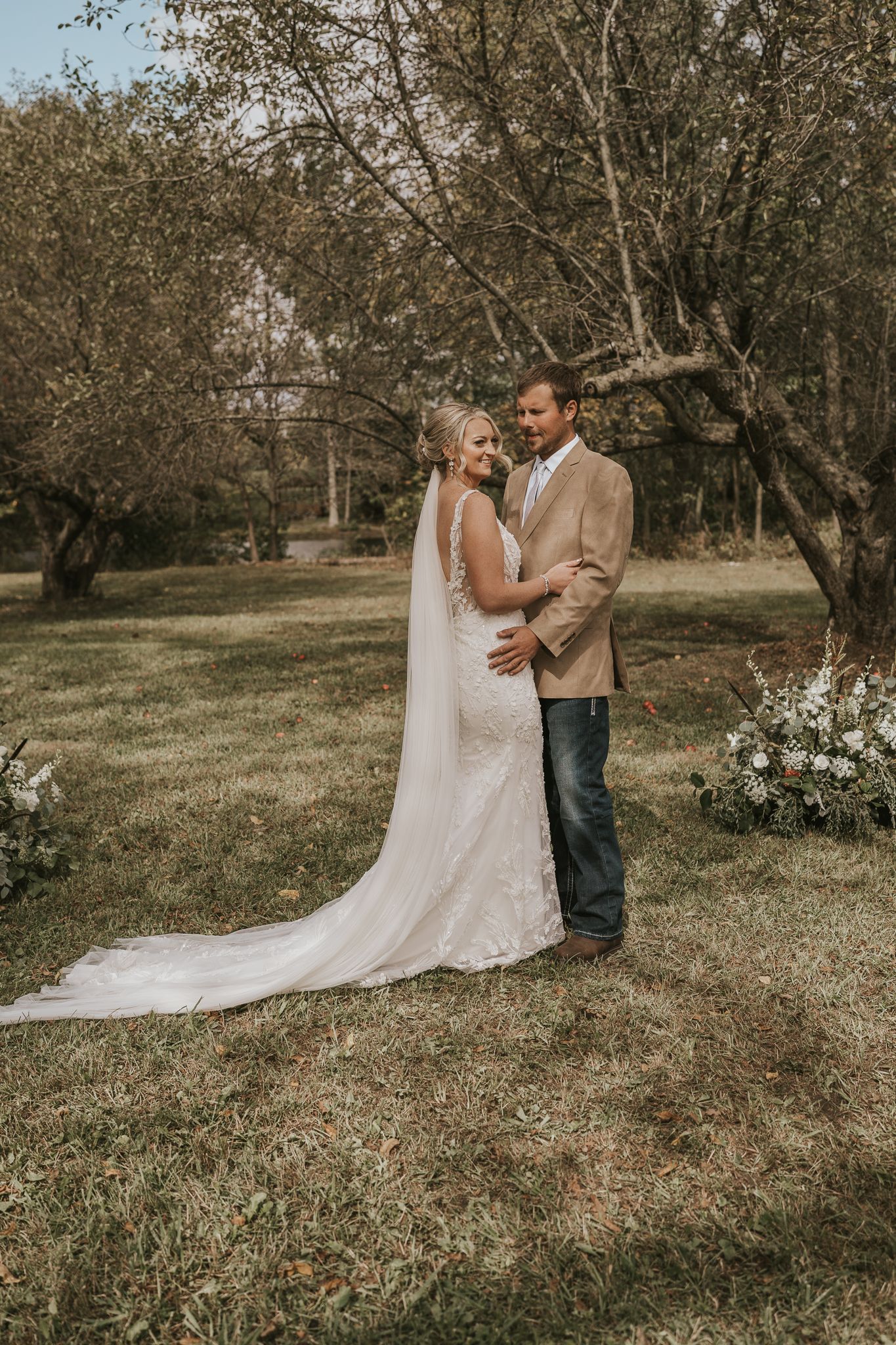 Couple shares joyful laughter during their first look in a sunlit orchard.