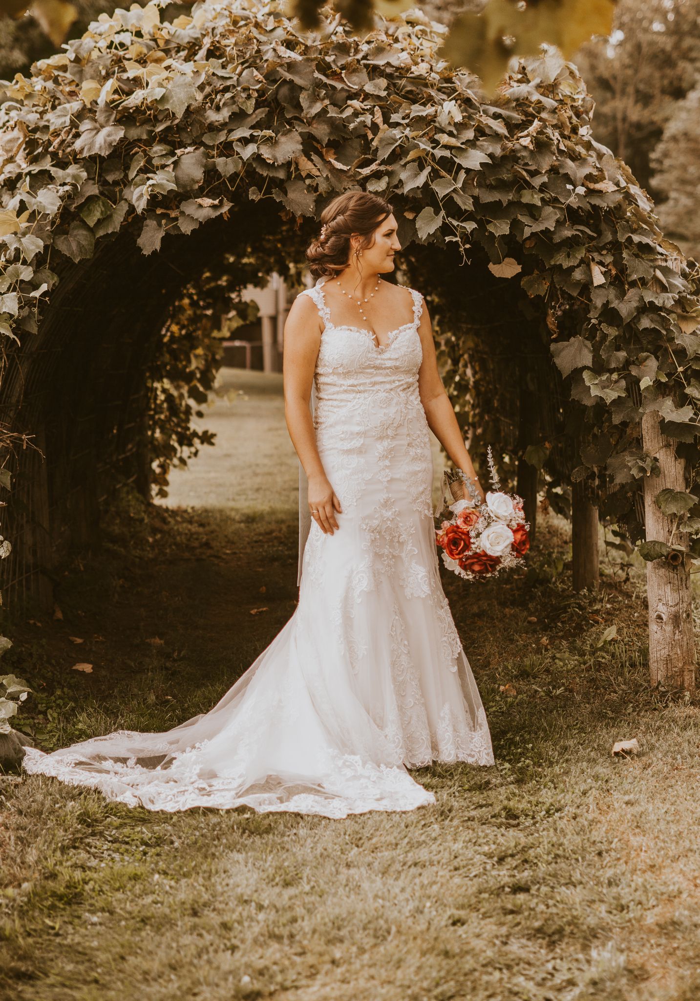 A bride poses with her bouquet under a natural vine-covered garden archway.
