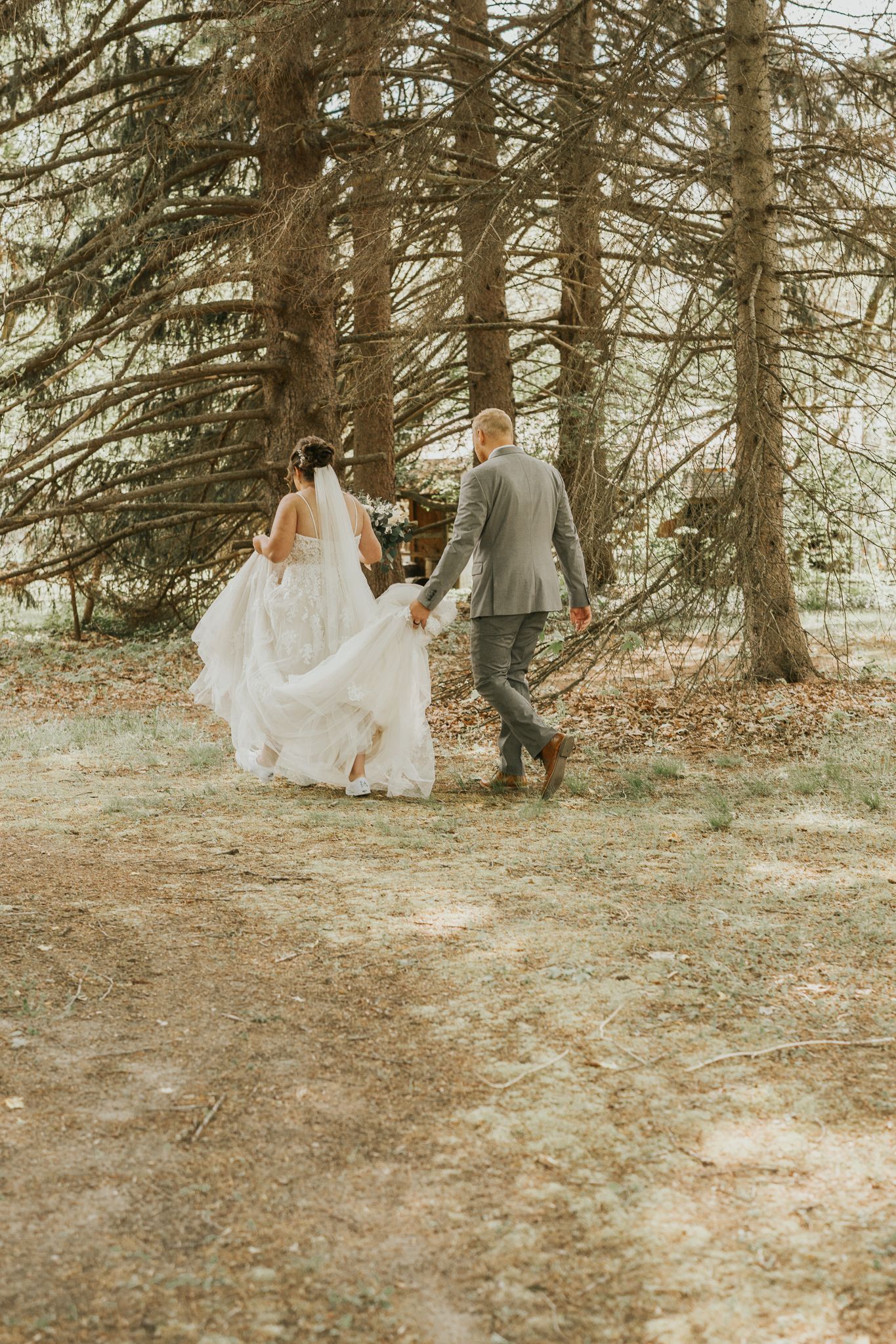 A couple walks hand in hand through a forest path in wedding attire.