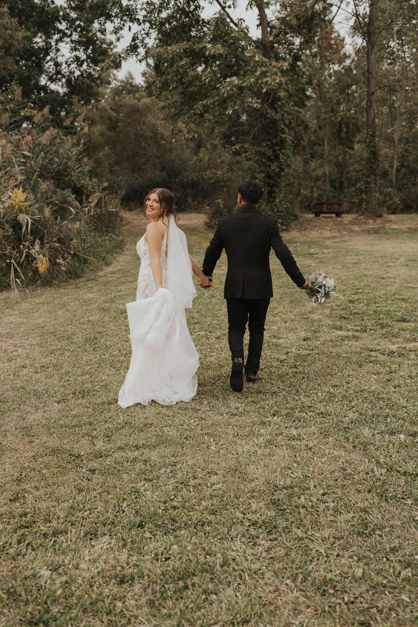 Newlyweds walking together across a scenic grassy field.