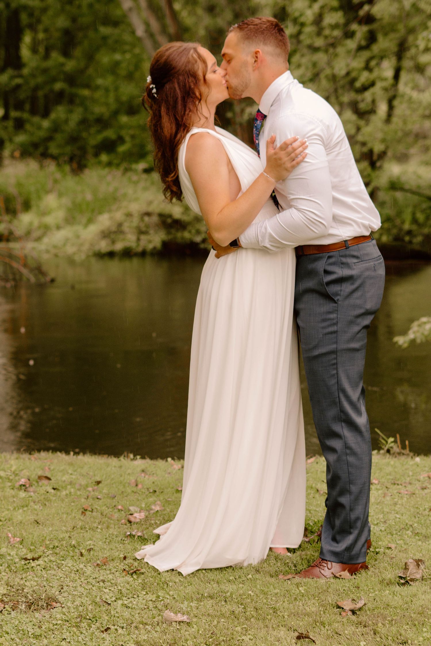 Couple shares romantic moment during outdoor wedding photoshoot by lake.