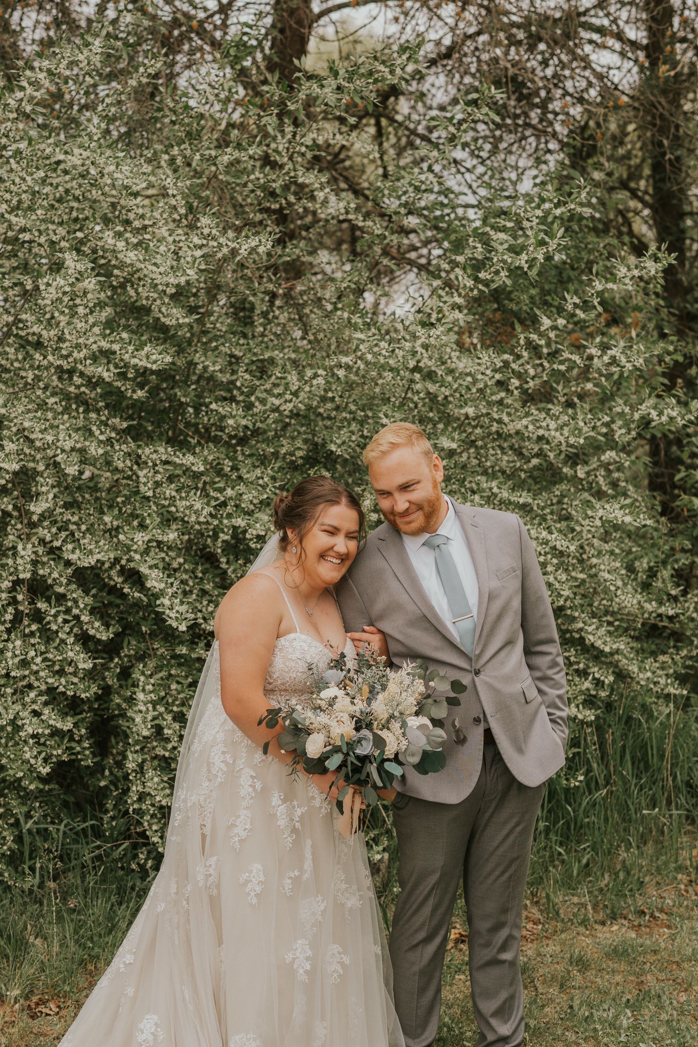 Wedding couple sharing joyful moment surrounded by blooming spring trees.