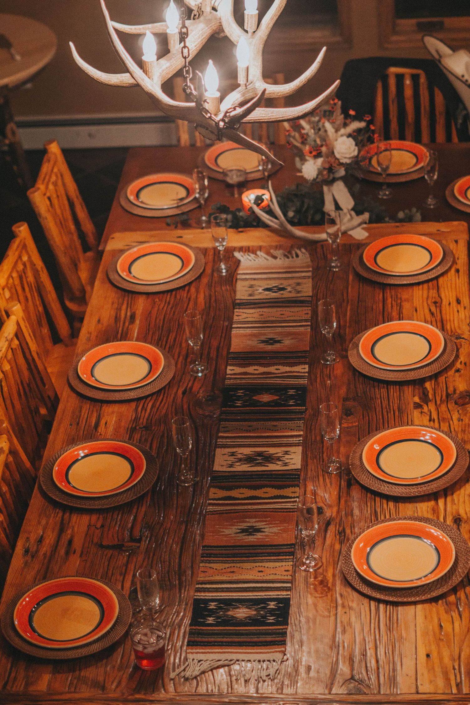 Rustic table setting with orange-rimmed plates and antler chandelier for a wedding reception.