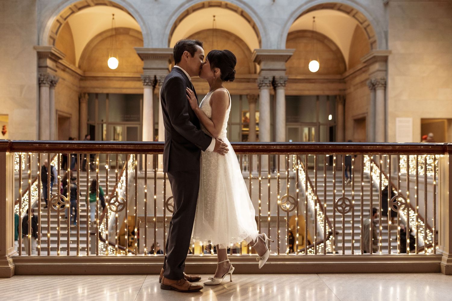 Couple embracing on an elegant balcony with classical architecture and arched columns.
