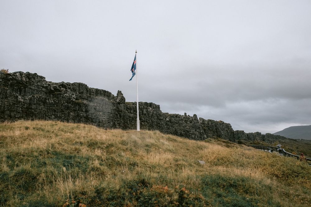 A flag waves on a hilltop against an overcast sky with rolling hills in the background.