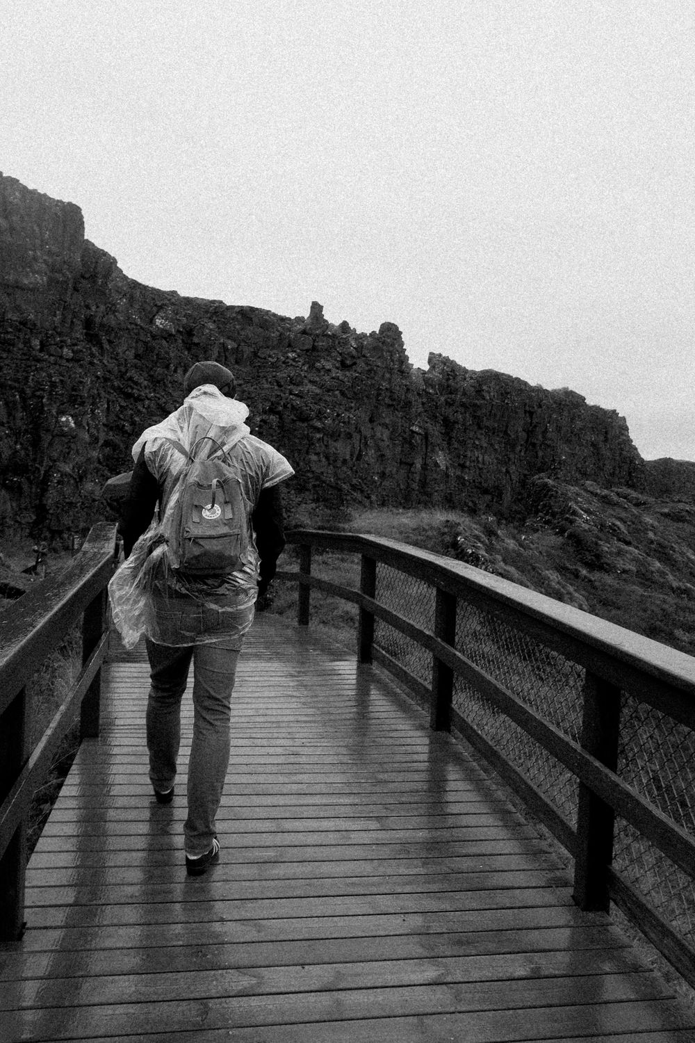 A person walks along a wooden boardwalk path through rocky terrain in black and white.