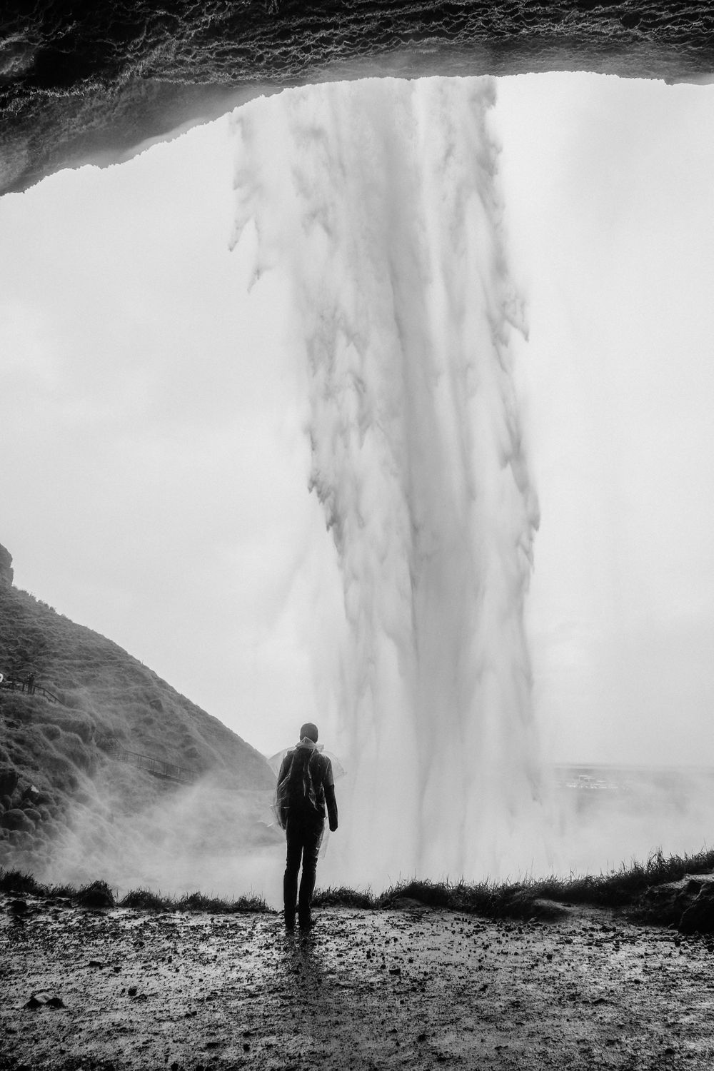 Silhouetted figure stands near powerful waterfall creating dramatic misty atmosphere.