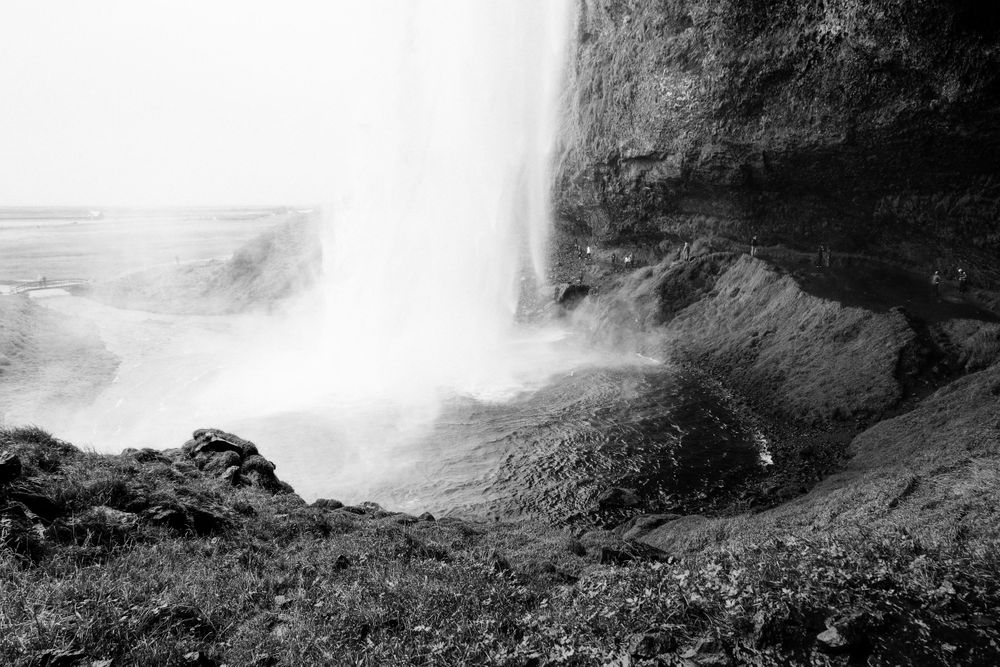 Massive waterfall creates misty spray as it plunges down a steep rocky cliff face.